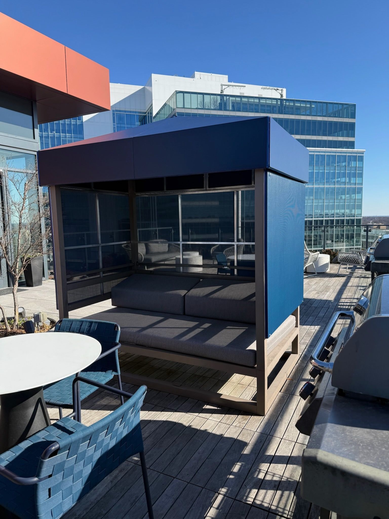 Blue rooftop cabana with lounge seating on a city rooftop terrace under a clear sky.