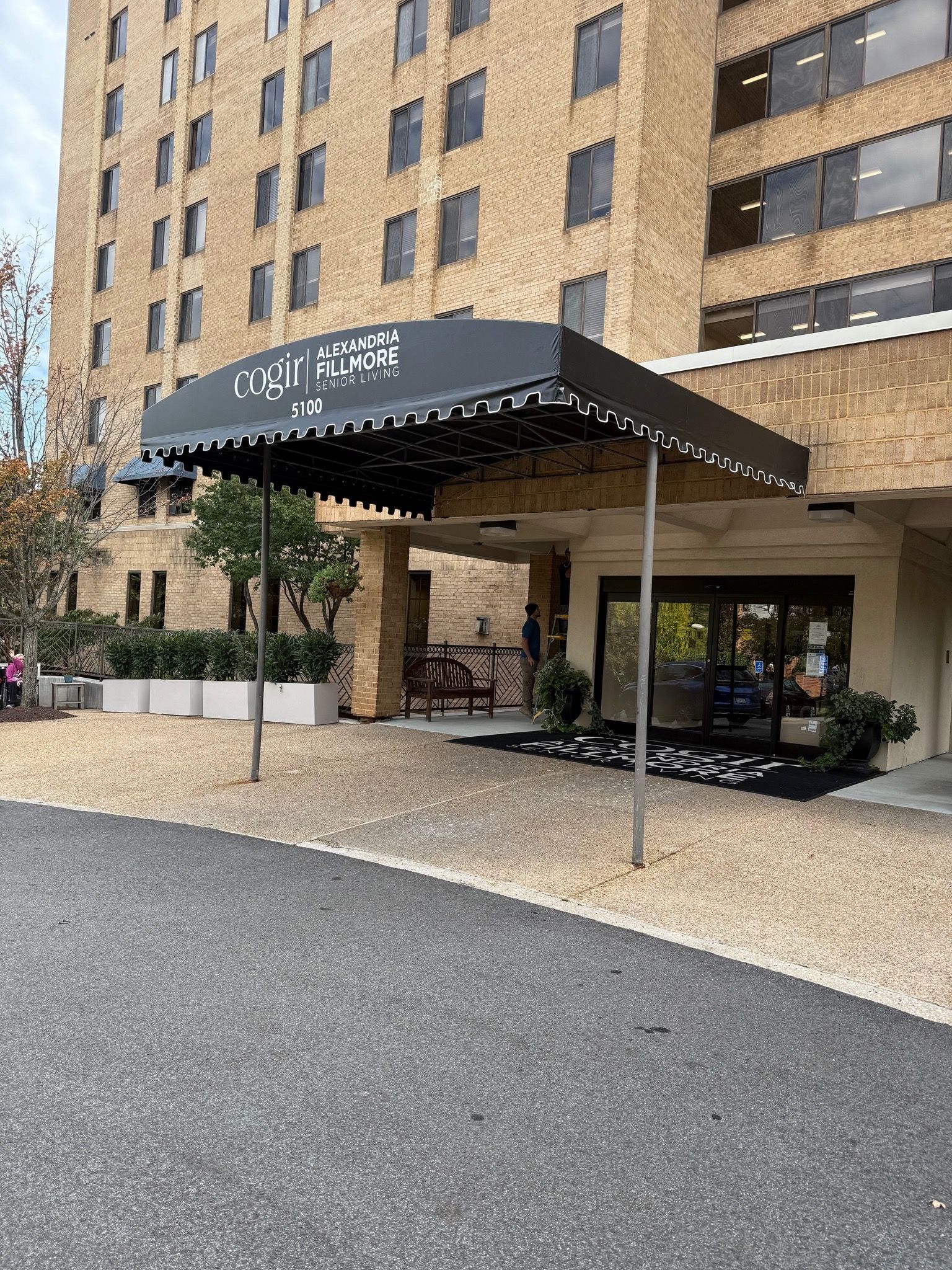 Hotel entrance with black awning, brick facade, and outdoor seating under the canopy.