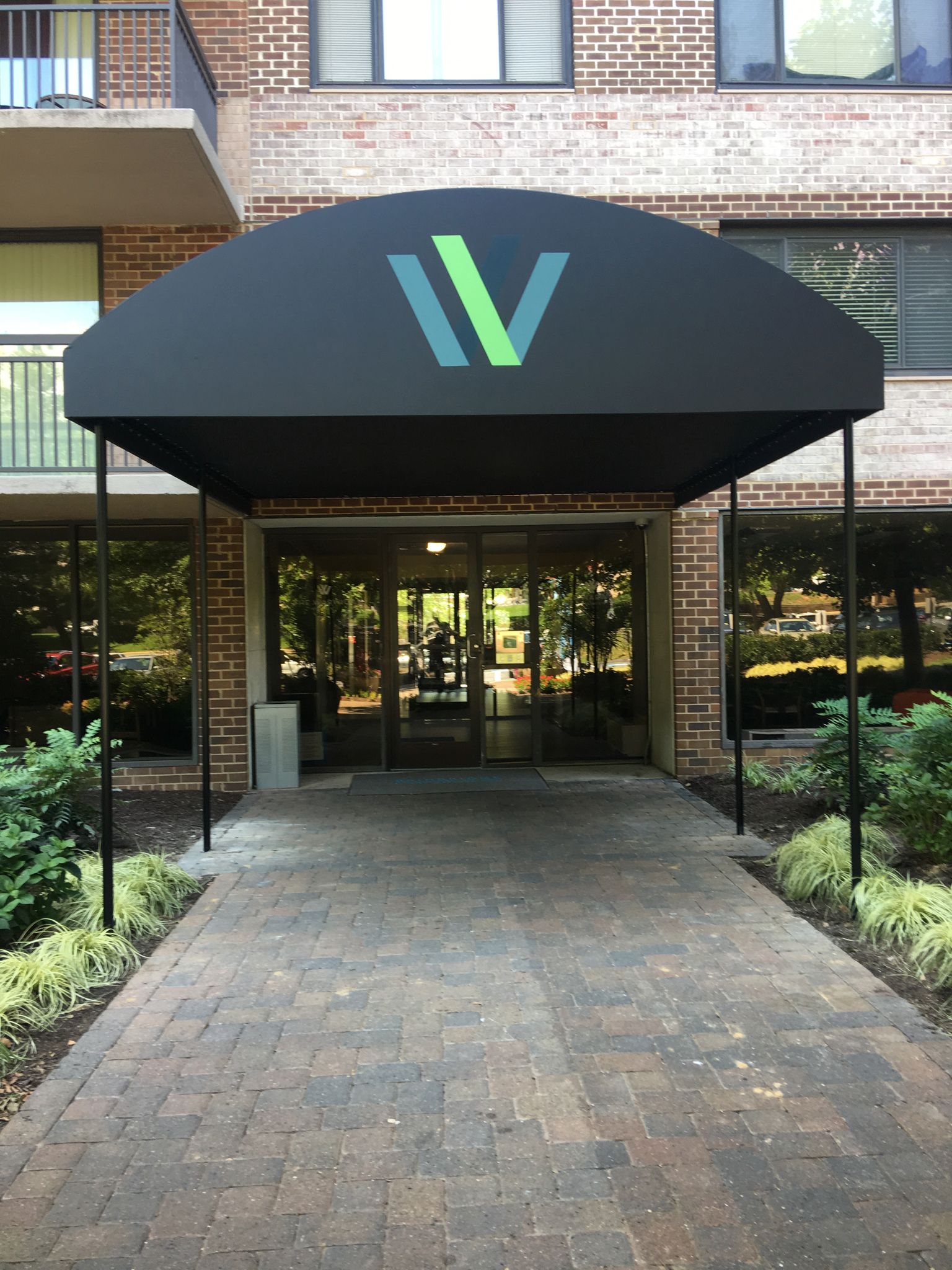 Building entrance with black awning and green-blue logo above a brick walkway.