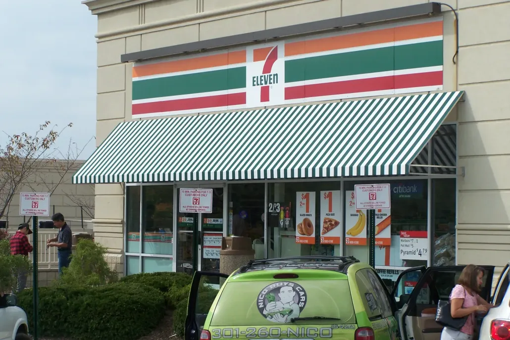 7-Eleven storefront with green-striped awning and parked cars out front