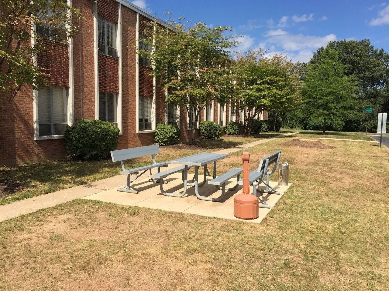 Outdoor picnic tables on a grassy lawn beside a brick building on a sunny day