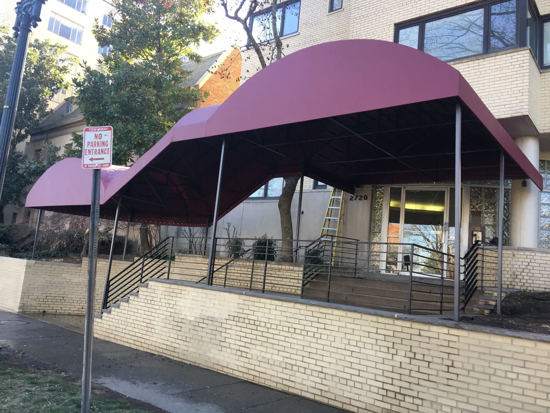 Purple canopy-covered outdoor walkway beside a brick building and chain-link fence