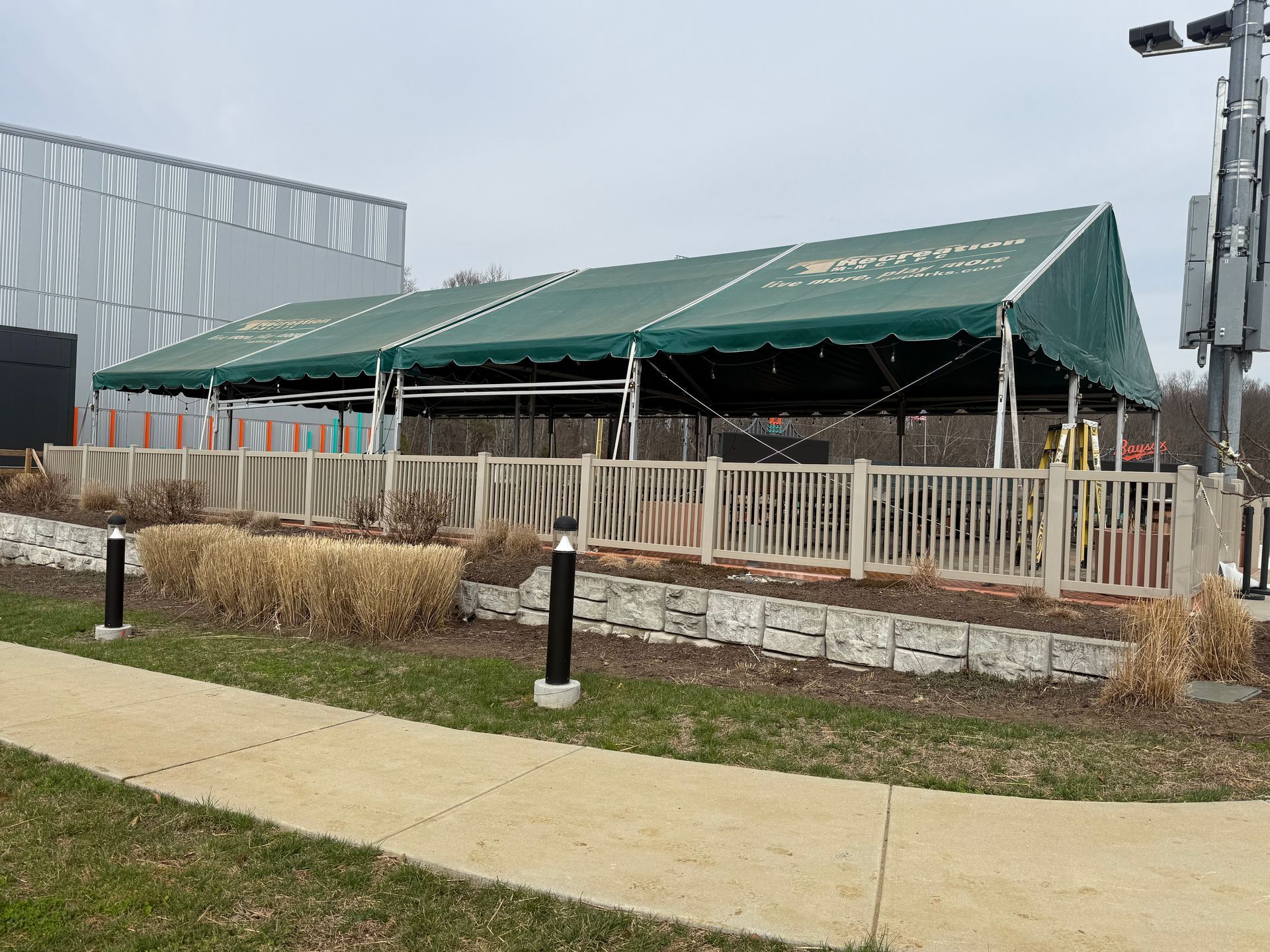 Outdoor patio construction with a green canopy, white fence, and sidewalk in front
