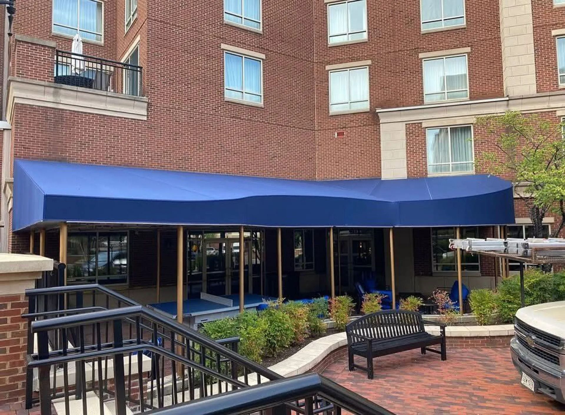 Brick apartment building with a blue awning over a patio and benches in a courtyard