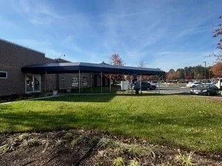 School building with covered entrance, green lawn, and parked cars under a blue sky