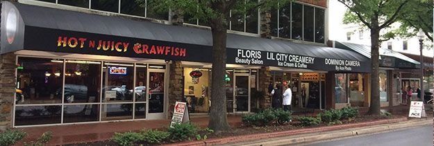 Street view of storefronts, including Hot N Juicy Crawfish, along a tree-lined sidewalk.