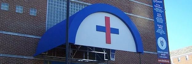 Blue hospital entrance canopy with a red cross on a brick building