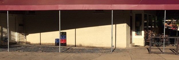 Strip mall storefront with beige walls, maroon awning, and a blue vending machine outside