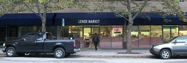 Storefront with a blue awning and two parked cars on a tree-lined street.