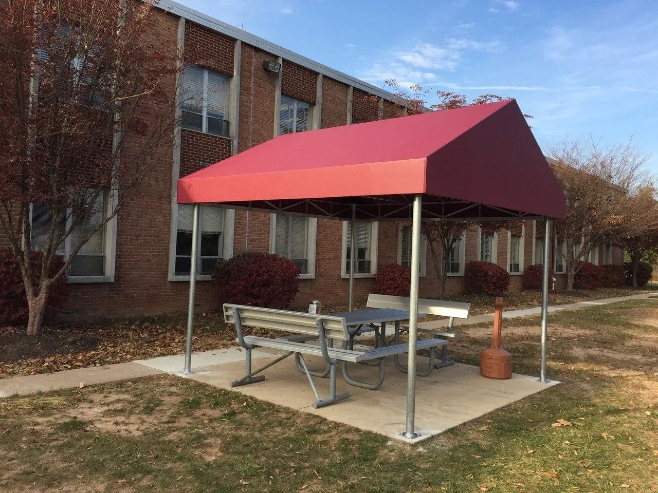 Covered outdoor picnic table beside brick building with a red canopy and benches