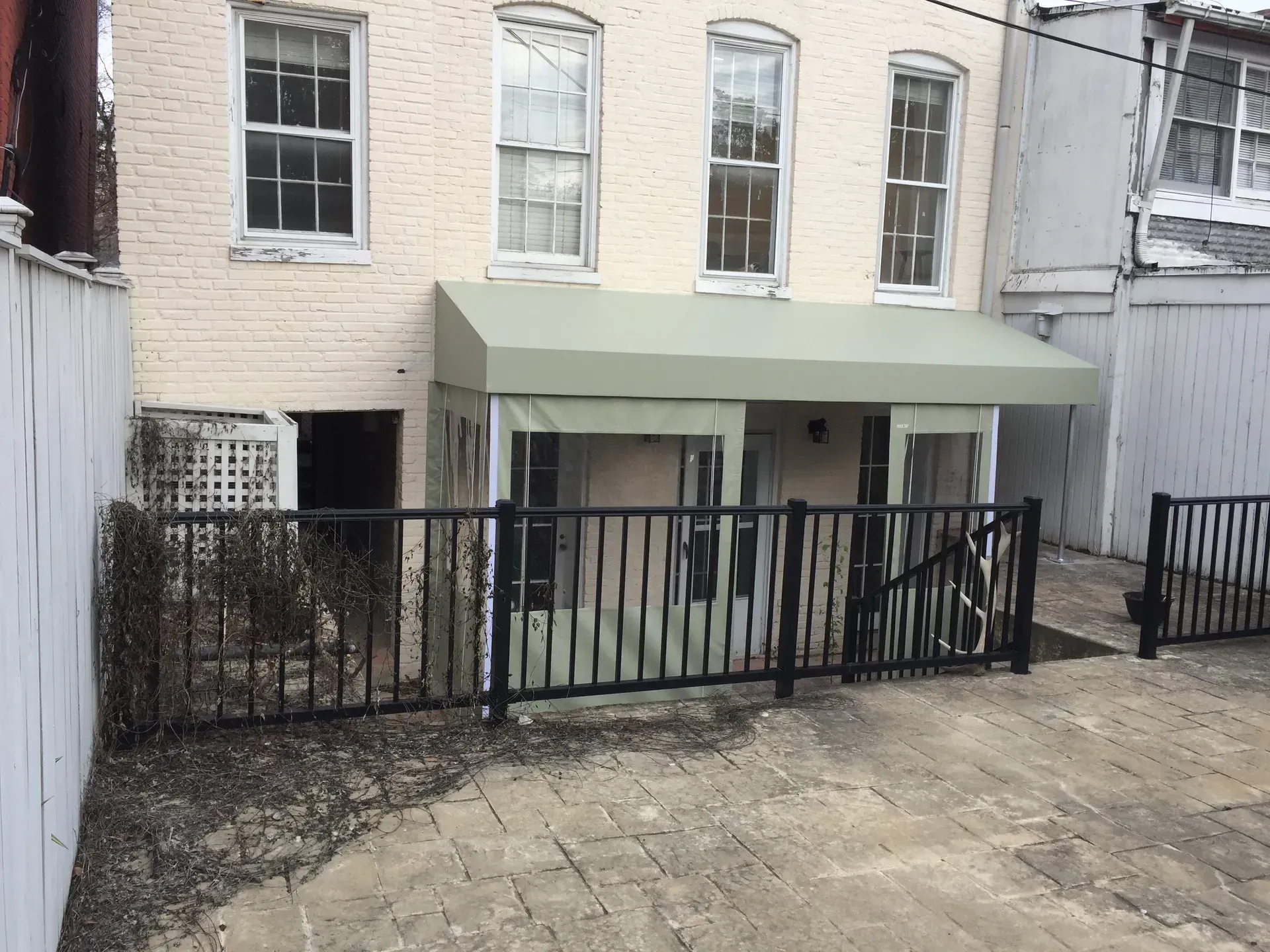Small brick building with a pale green awning and black metal fence in front