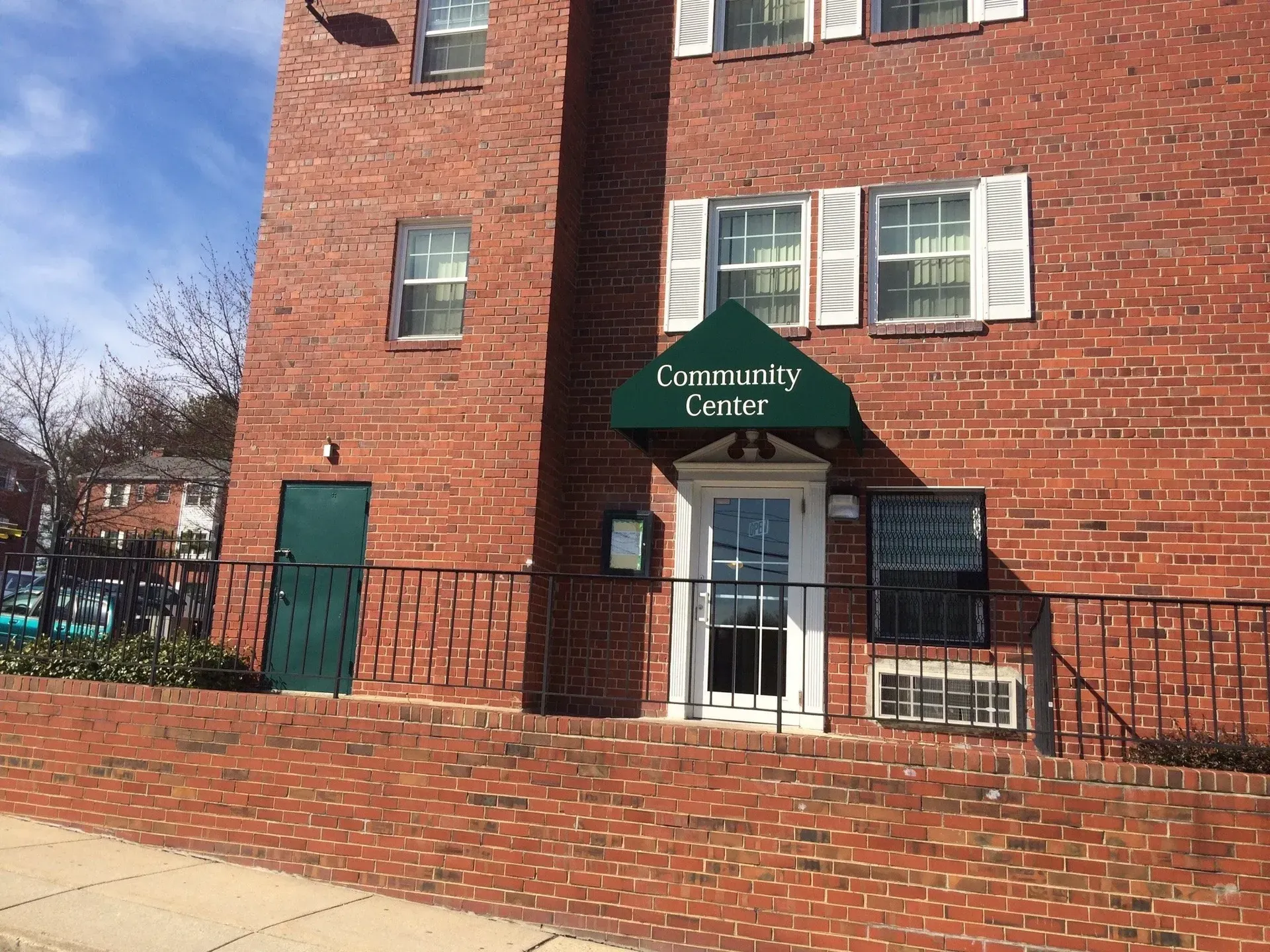 Brick building entrance with green awning labeled “Community Center” and a brick wall in front.