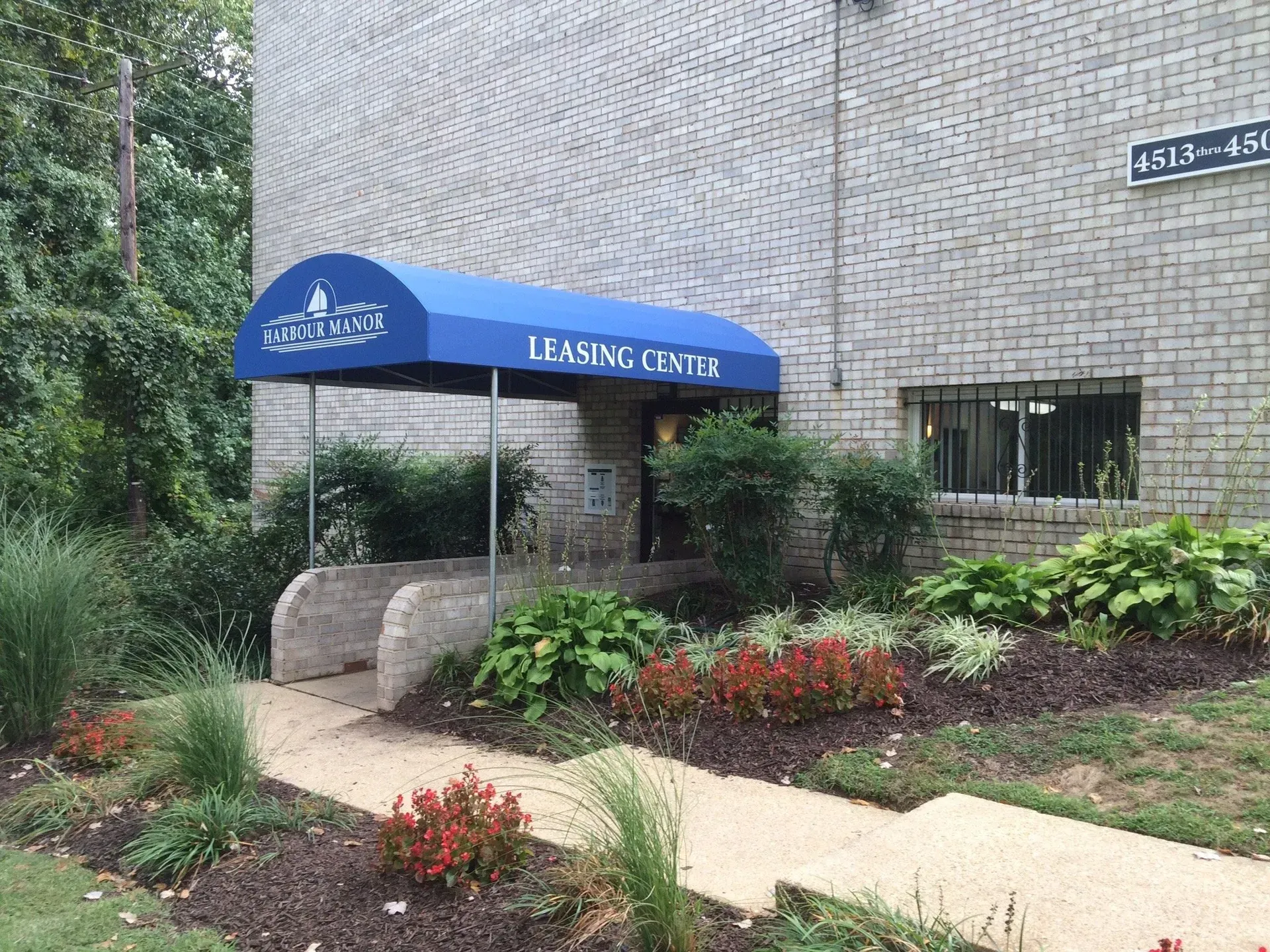 Leasing center entrance with blue awning, brick building, and landscaped walkway