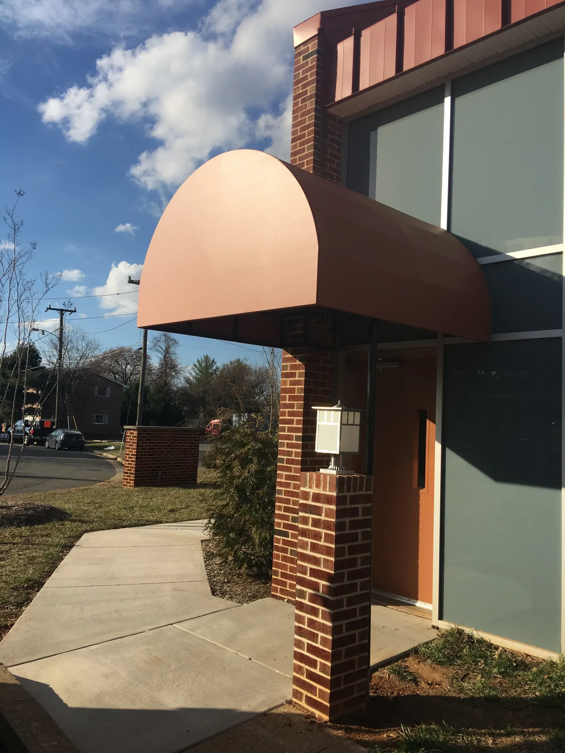 Brick building entrance with a tan awning over a sidewalk on a sunny day