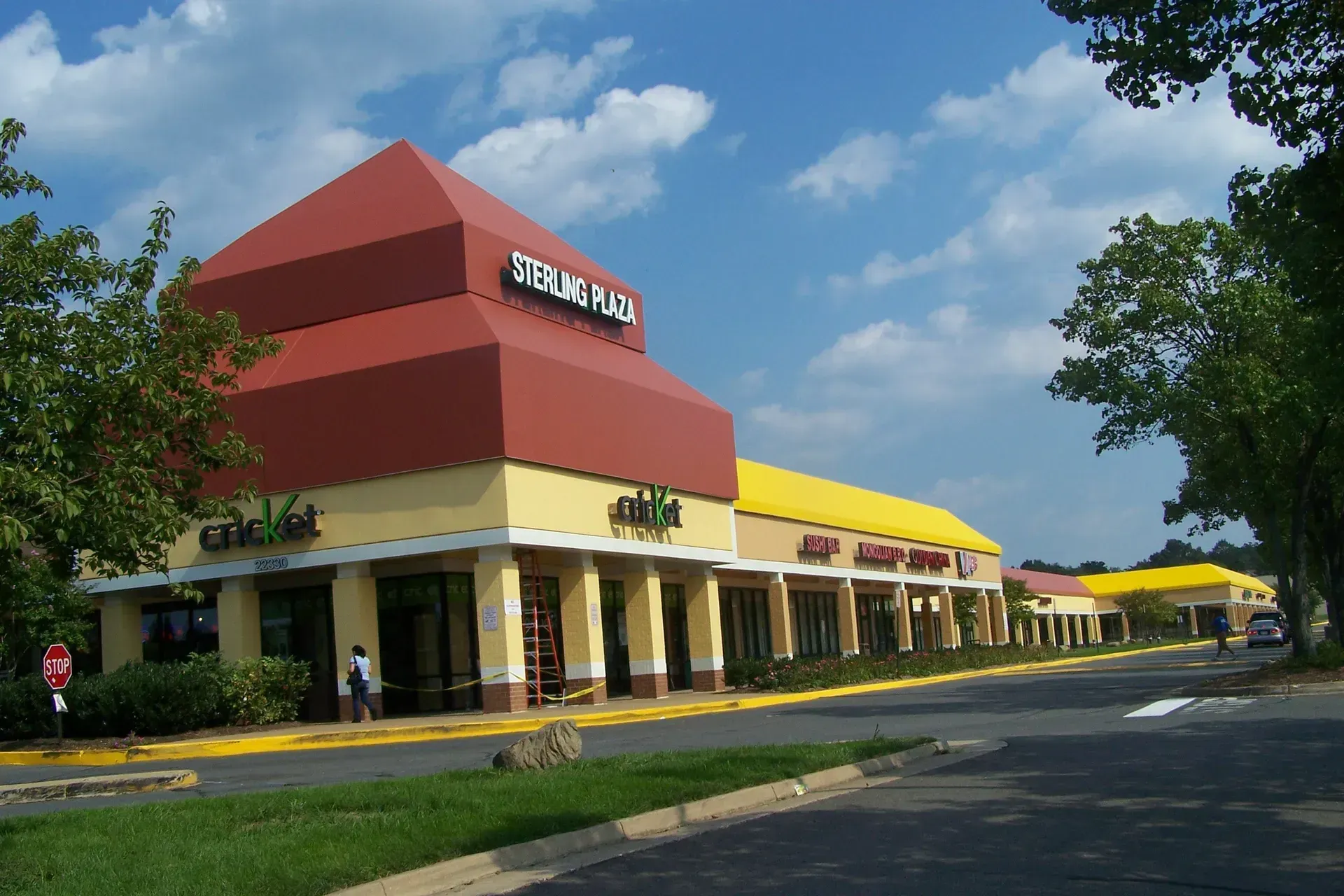 Shopping center with red and yellow roofs on a sunny day, viewed from the parking lot.