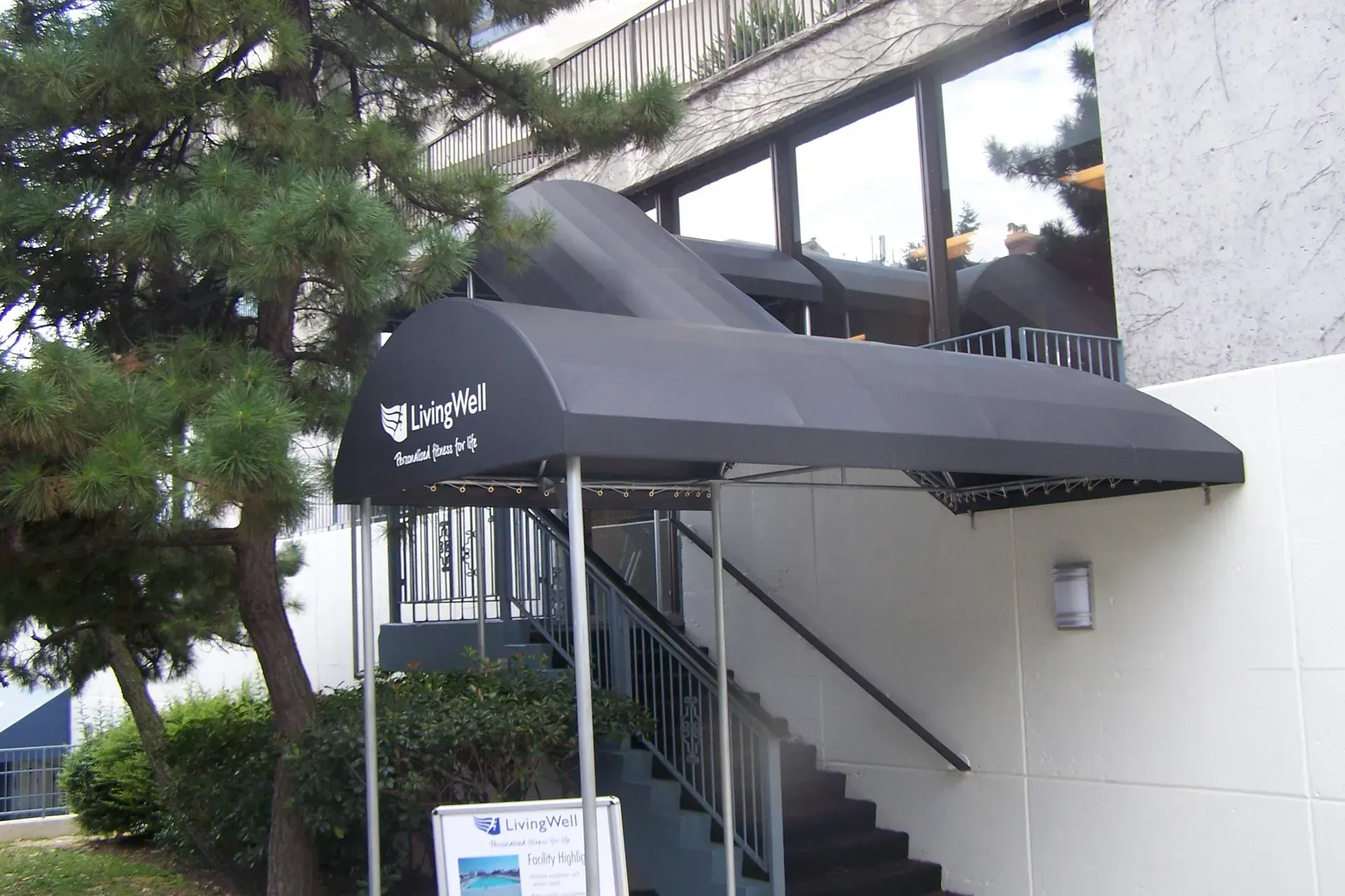 Covered staircase entrance with black awning beside a white building and trees
