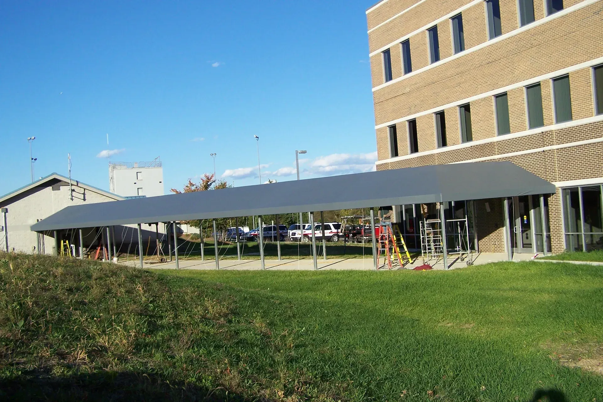 Long covered walkway beside a brick building on a grassy campus under a clear blue sky