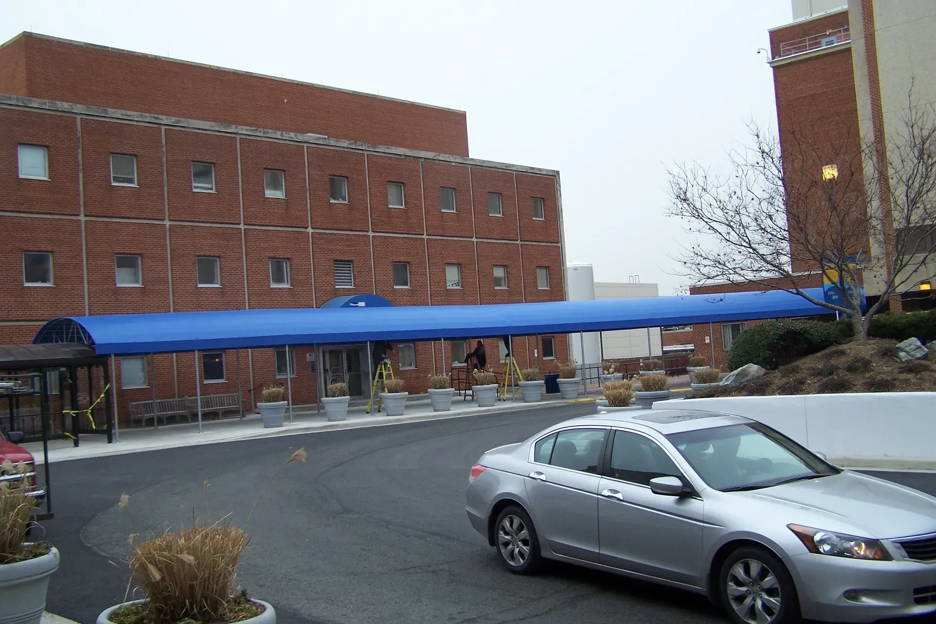 Brick building with blue awning over a snowy driveway, a silver car parked in front