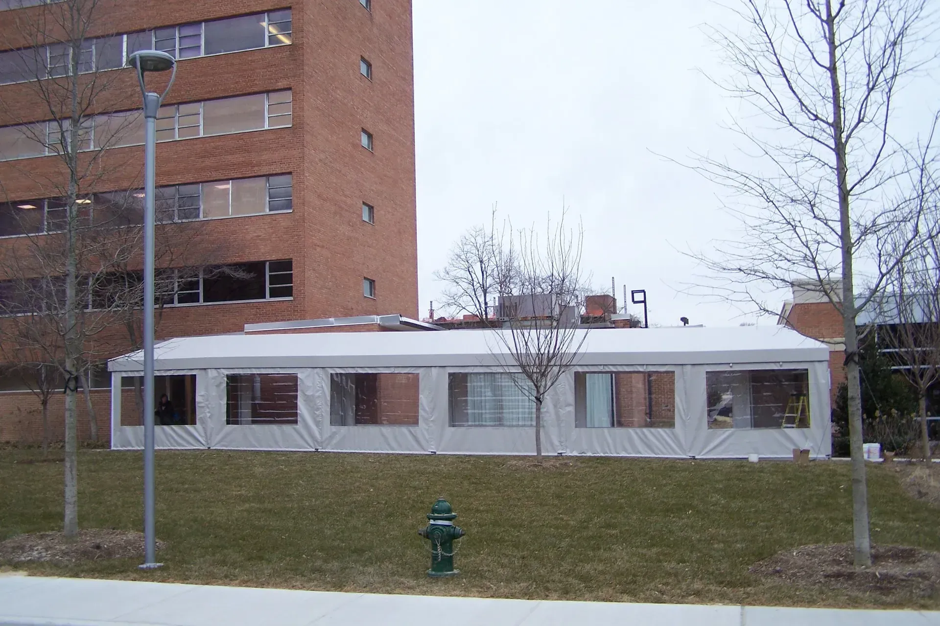 Low white building beside a brick building, with bare trees, grass, and a fire hydrant in front.