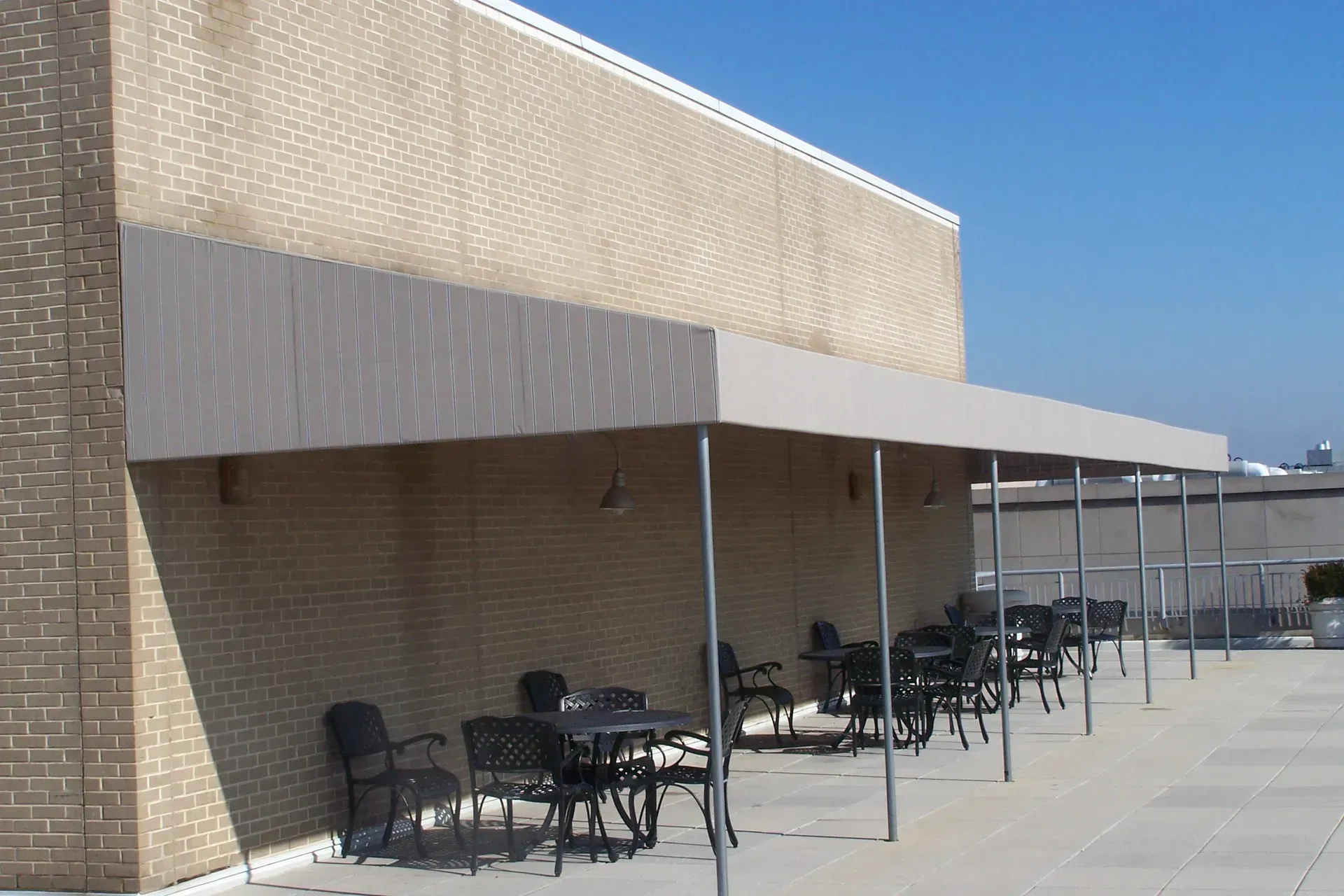Outdoor café seating beside a tan brick building under a white awning on a sunny day