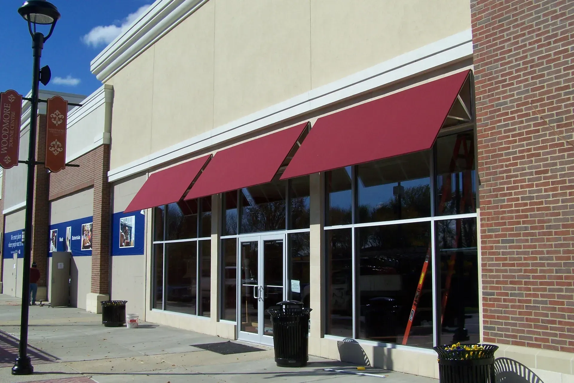 Storefront with red awnings and glass windows along a sunny sidewalk.