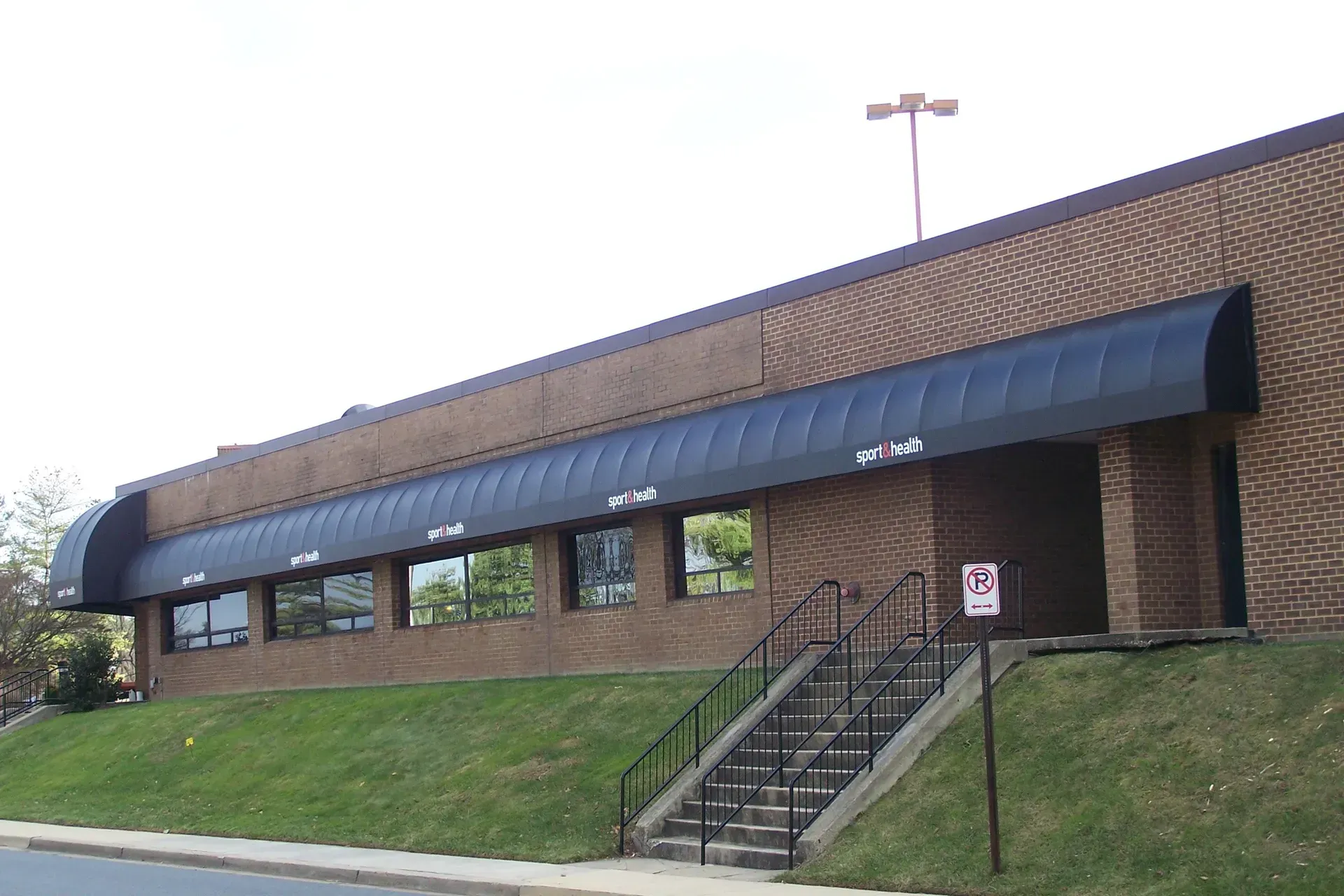 Brick building with blue awning, windows, and stairs leading to an entrance on a grassy slope.