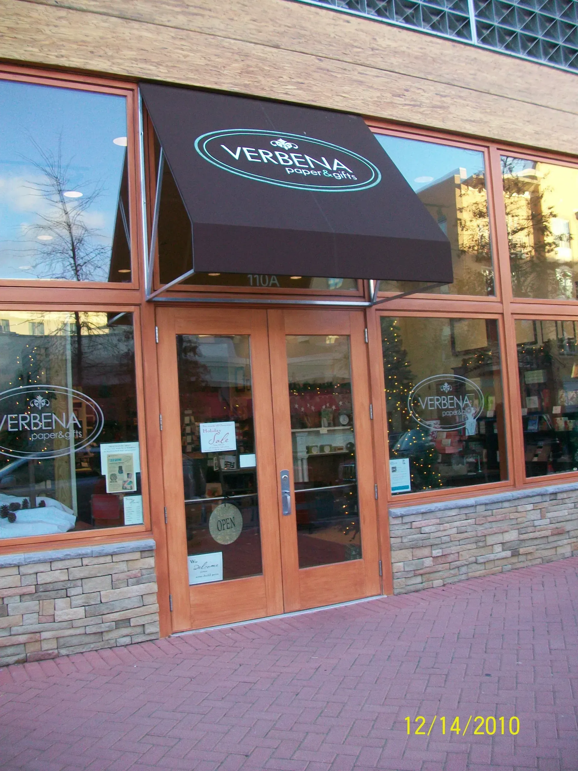 Storefront with wooden double doors, black awning, and large windows in a brick building.