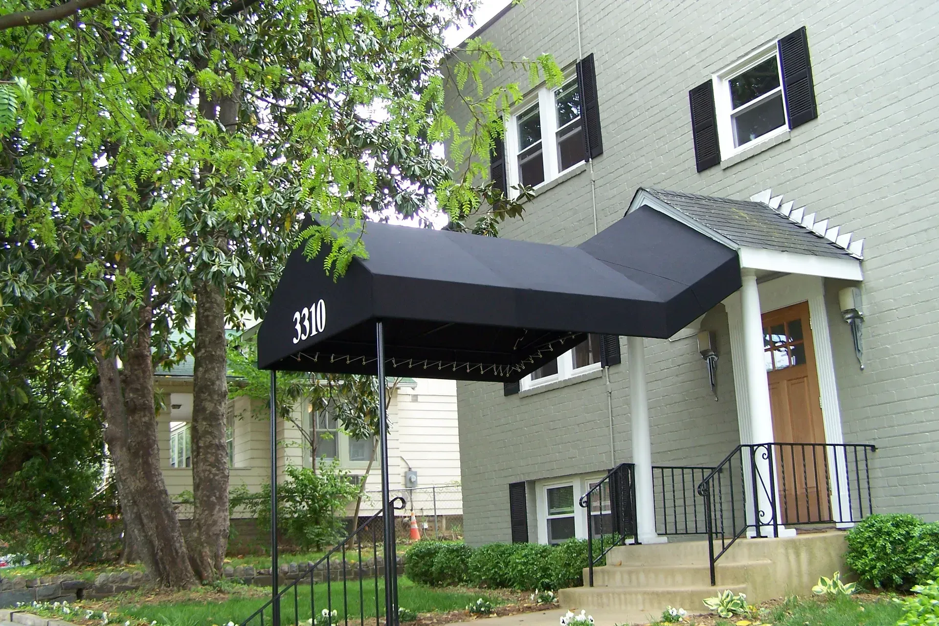 Apartment entrance with black awning and front steps, beside a tree and green lawn
