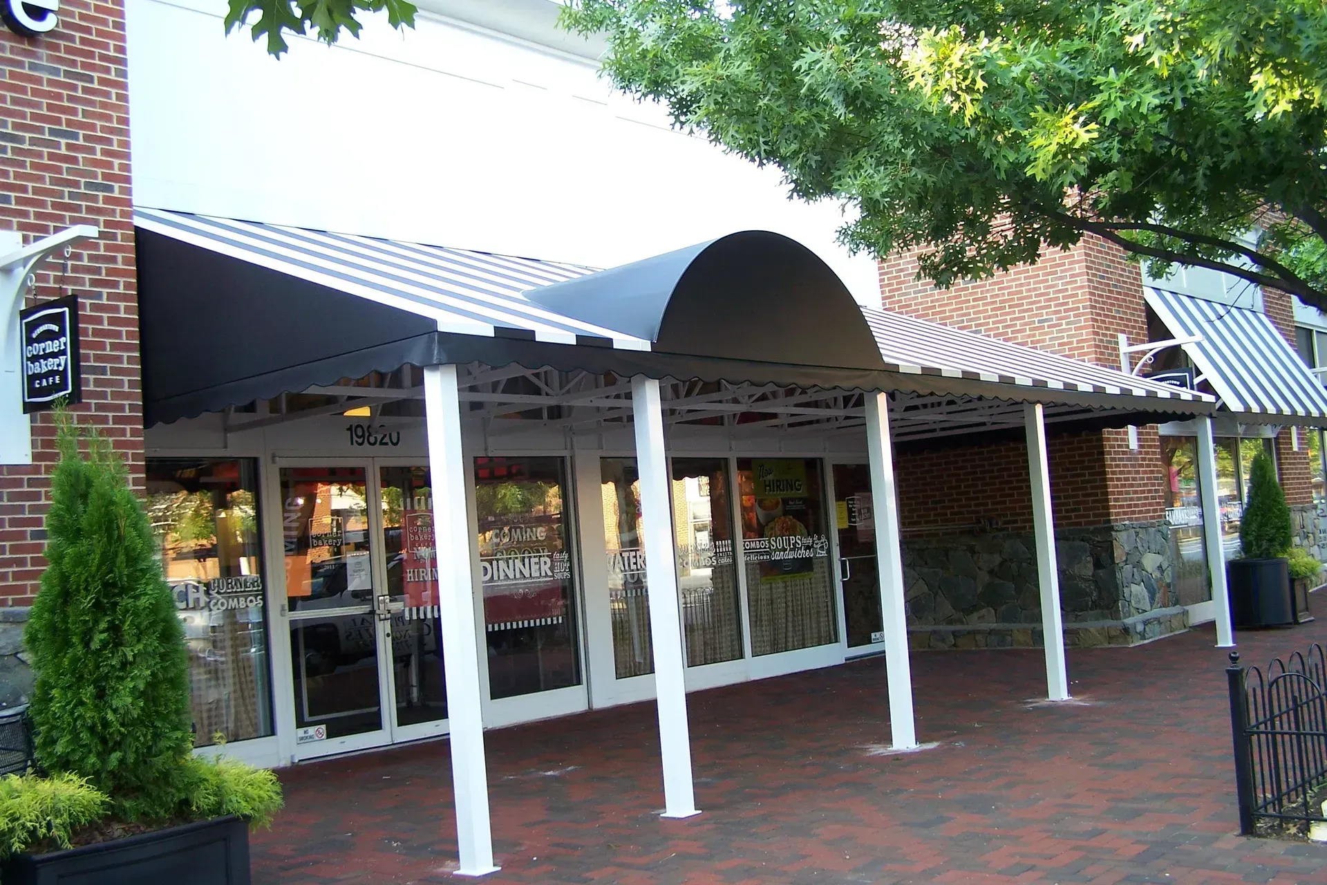 Storefront with glass windows, white columns, and a black awning along a brick walkway