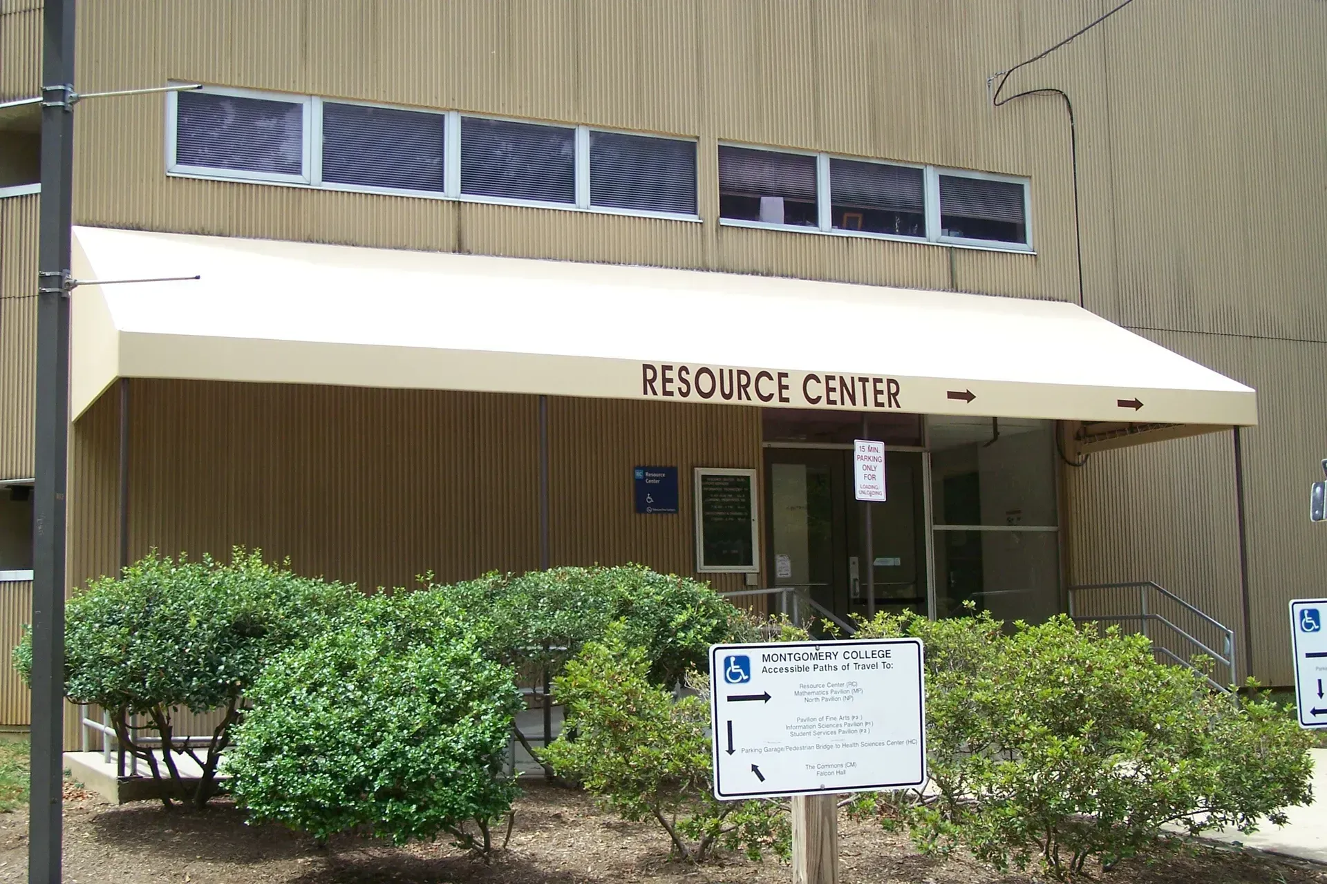 Resource Center building entrance with awning, windows, shrubs, and a sign in front.