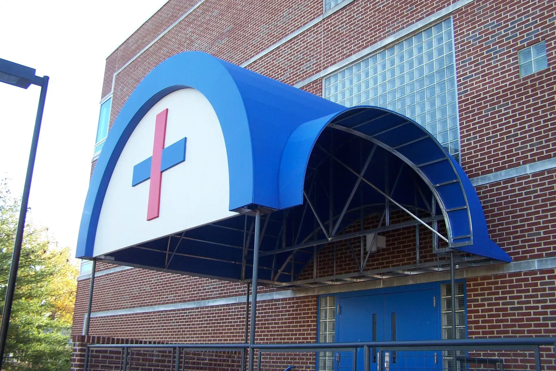Brick building entrance with a blue awning and a red cross sign