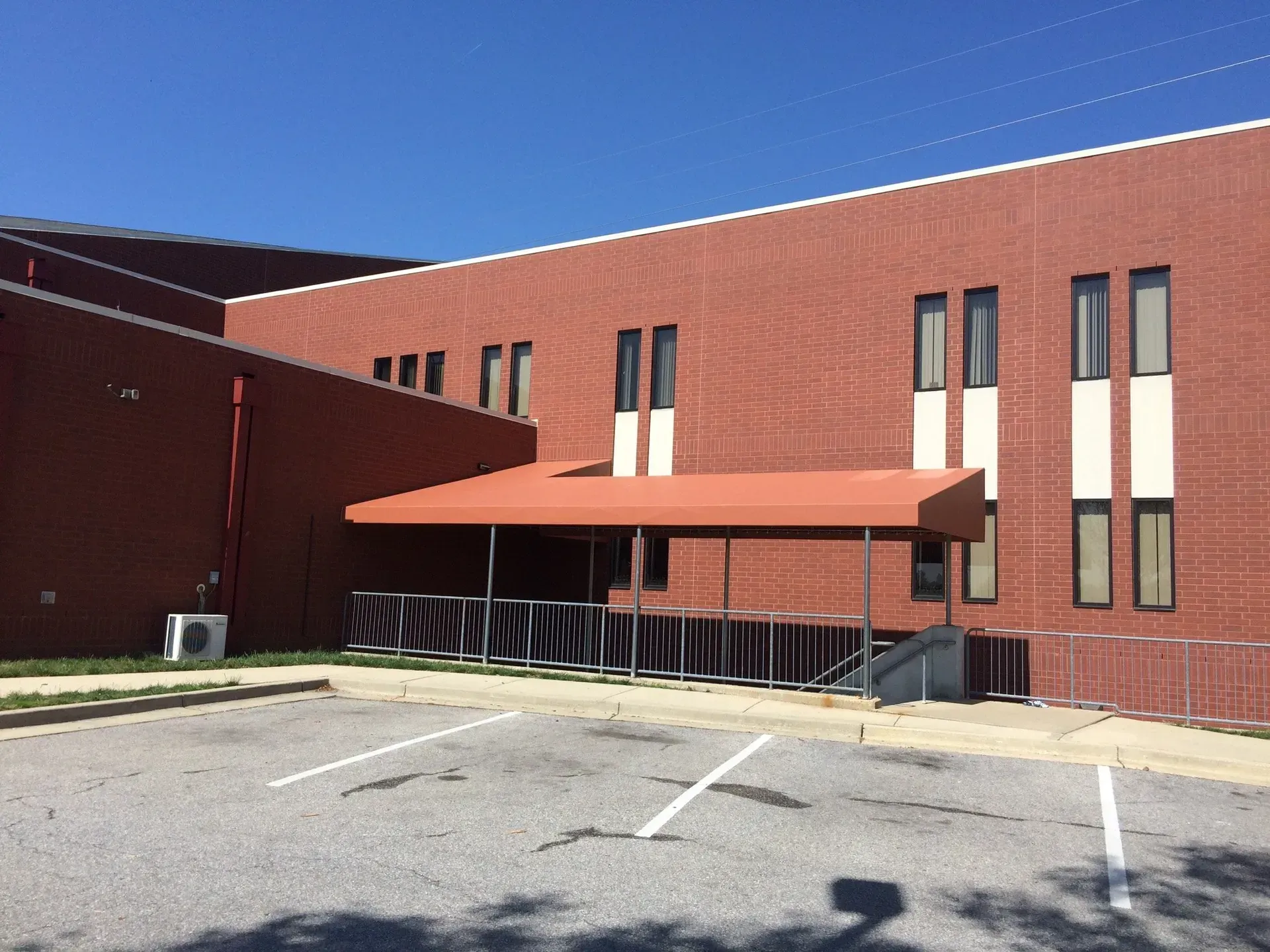 Red brick building with a covered entrance, tall narrow windows, and a parking lot in front