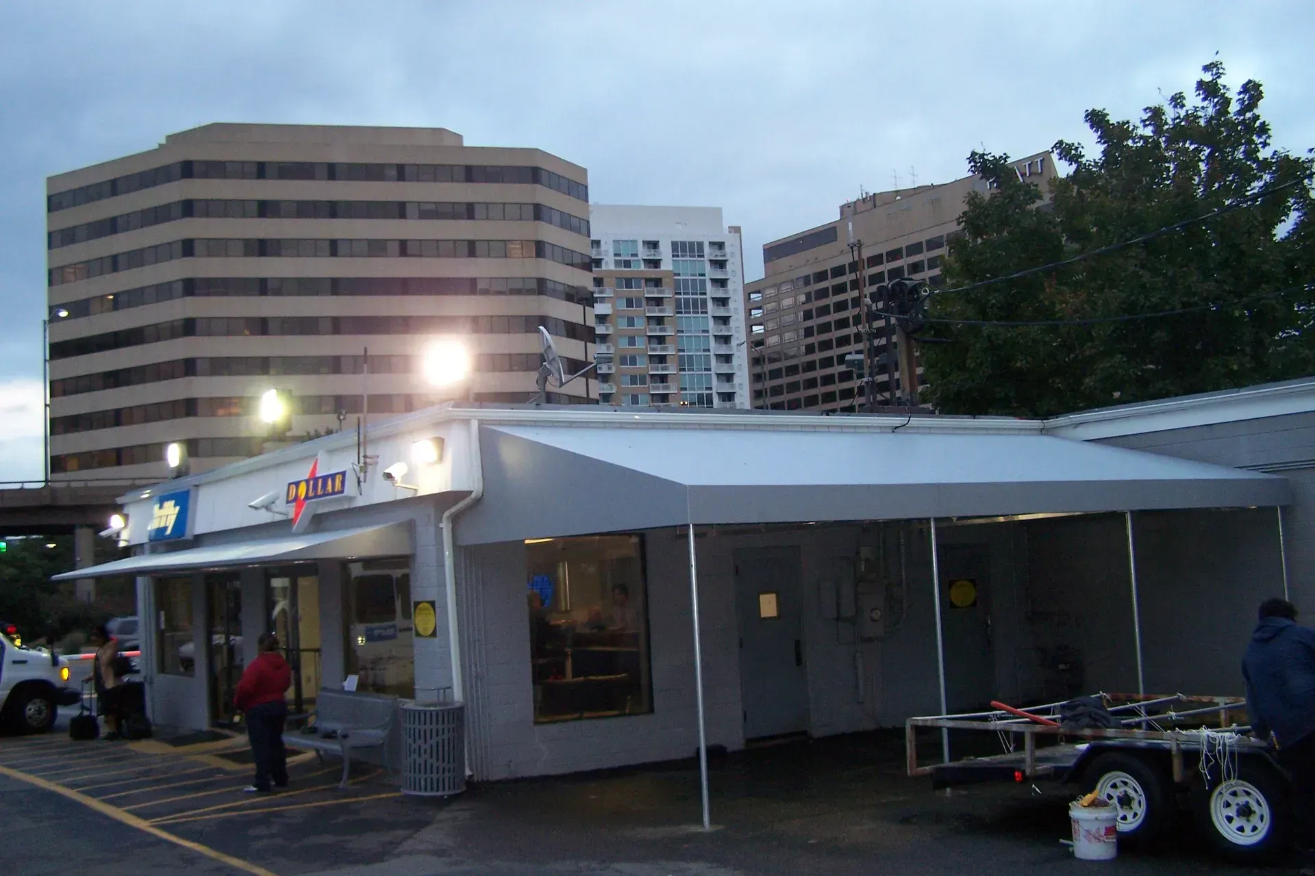 Outdoor market stall with white canopy in front of tall apartment buildings at dusk