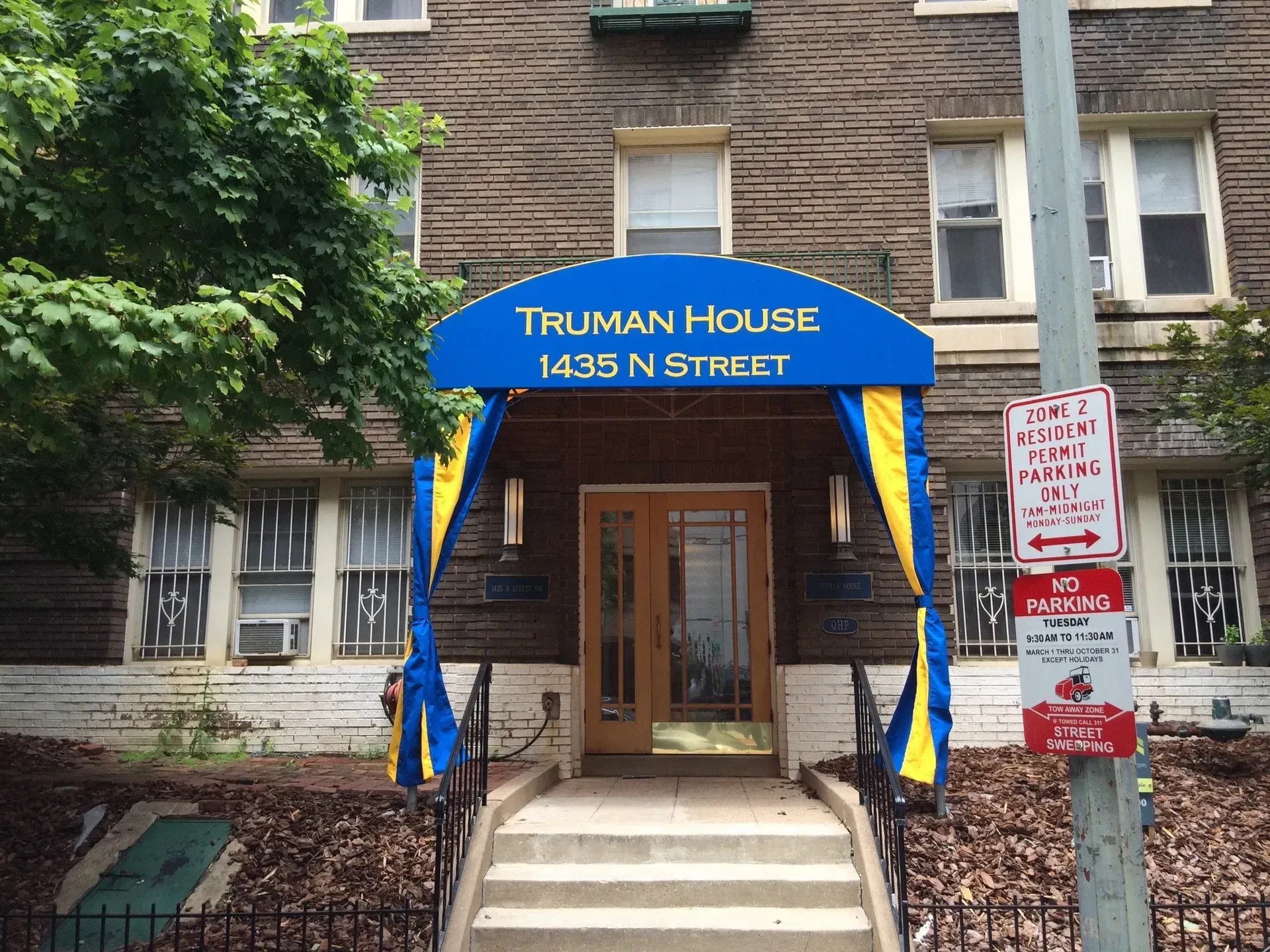 Truman House entrance with blue awning and stairs at 1435 N Street, framed by trees and brick walls