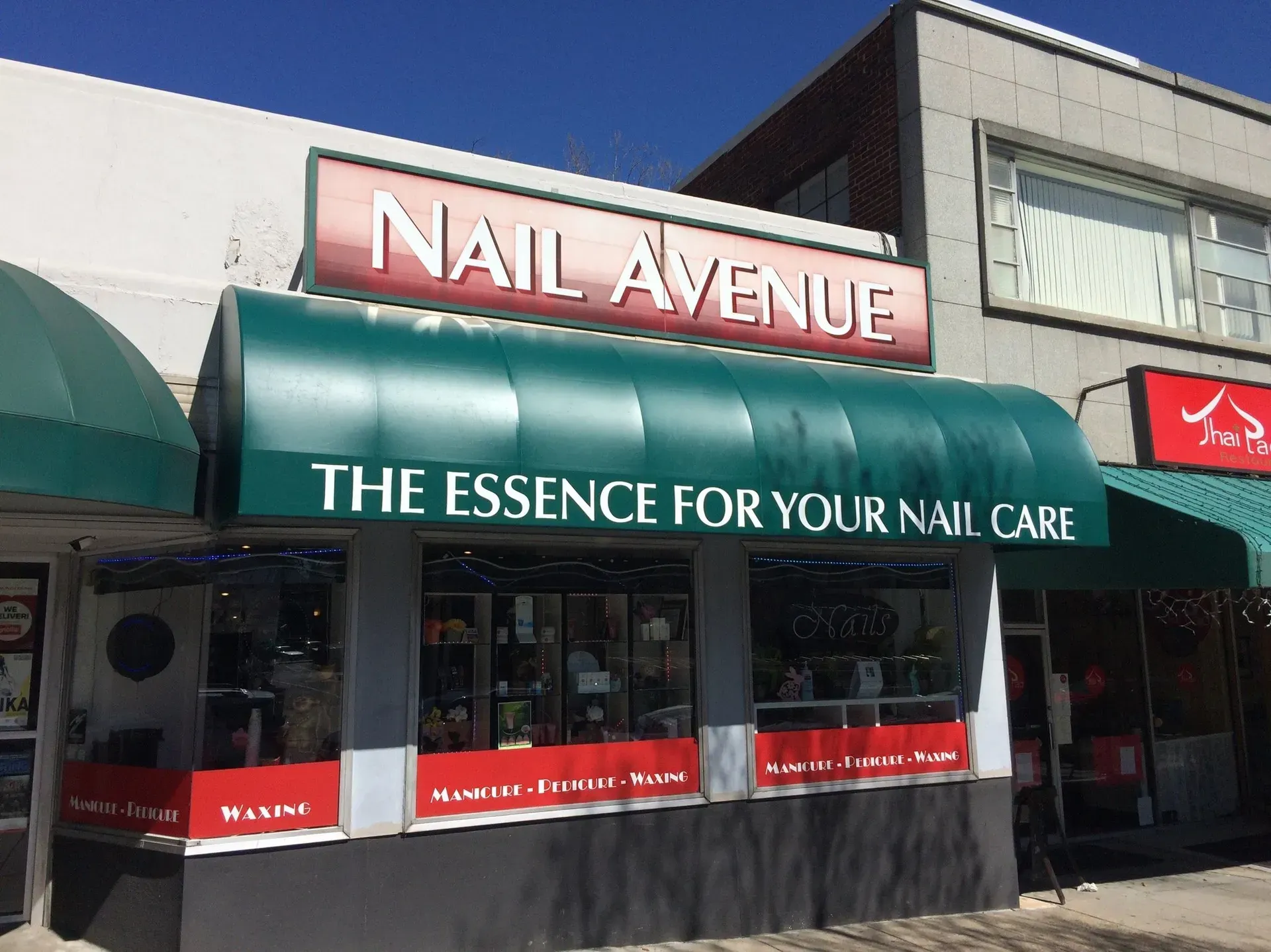 Storefront of Nail Avenue with green awnings and sign reading “The Essence for Your Nail Care”