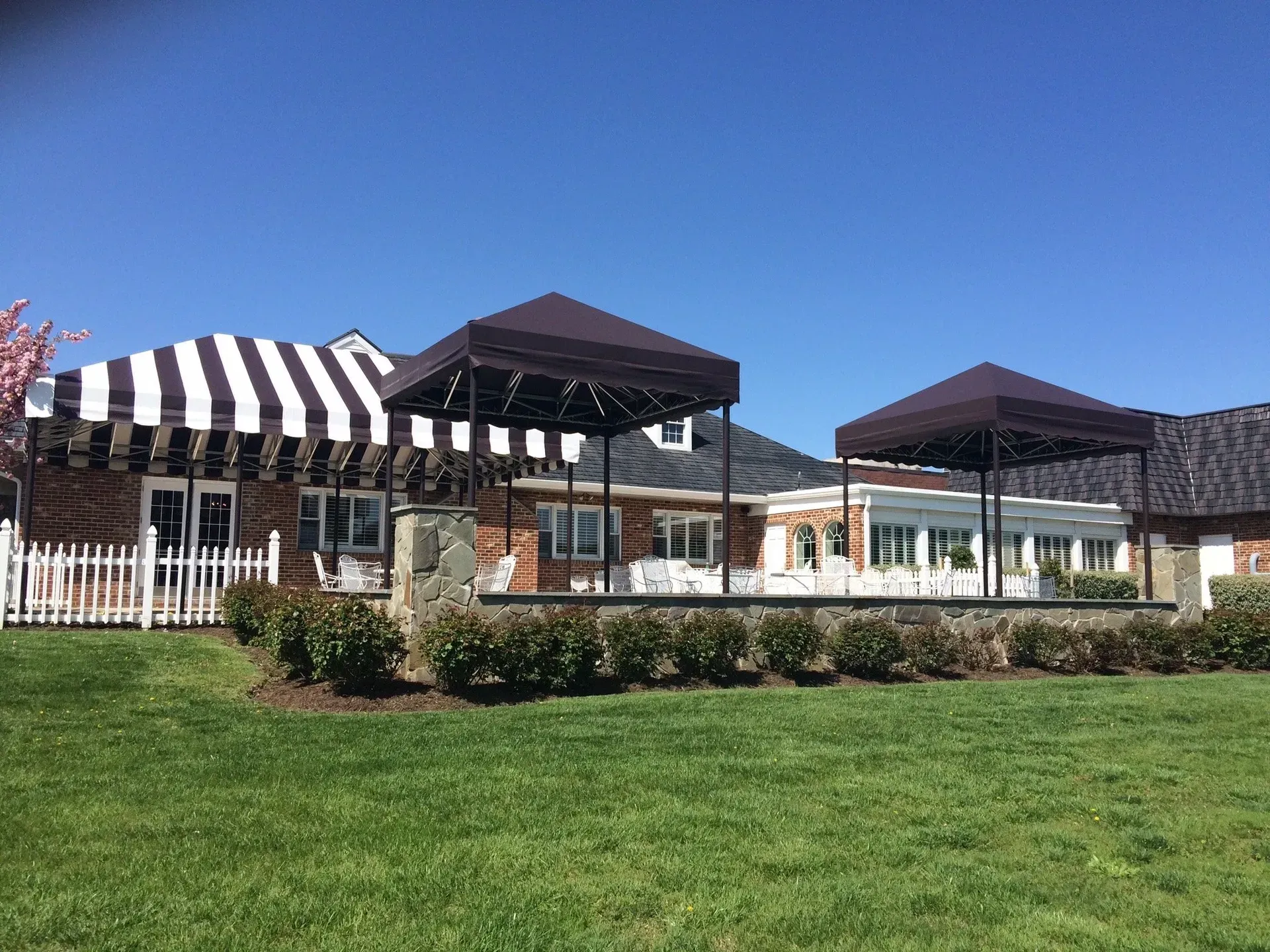 Outdoor patio with black-and-white striped awning, dark umbrellas, and a green lawn under a blue sky
