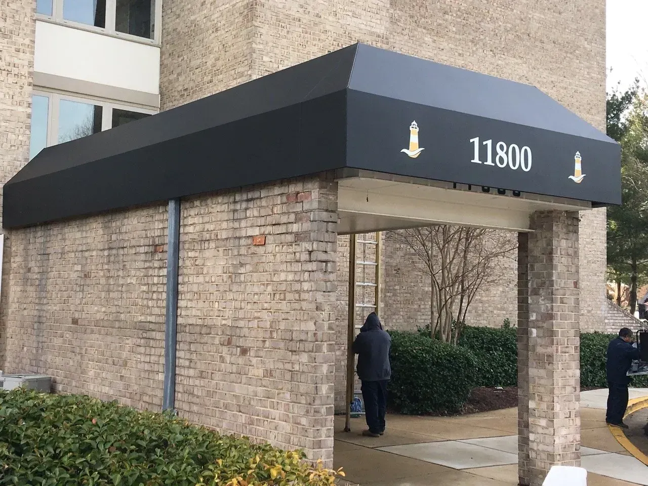 Covered apartment entrance with brick walls, black awning, and the number 11800 above the doorway