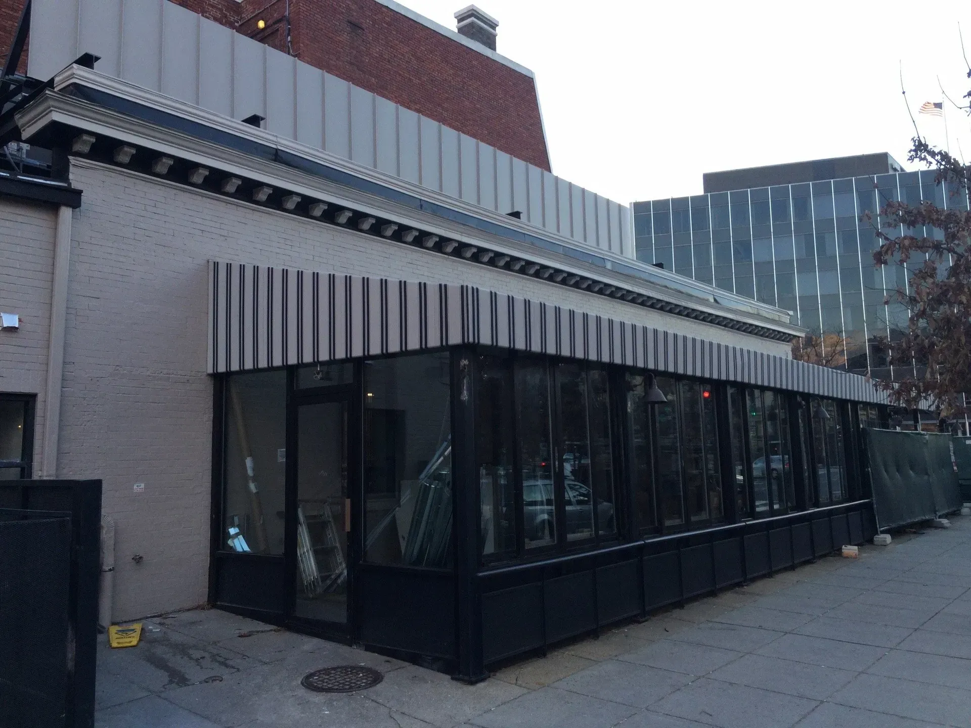 Modern storefront with black-framed windows and striped awning along a sidewalk