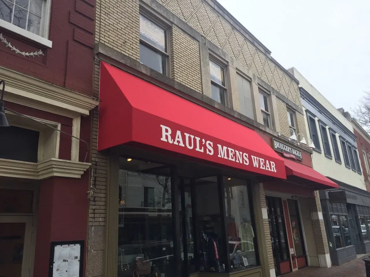 Storefront with a red awning reading “RAUL’S MEN’S WEAR” on a city street.