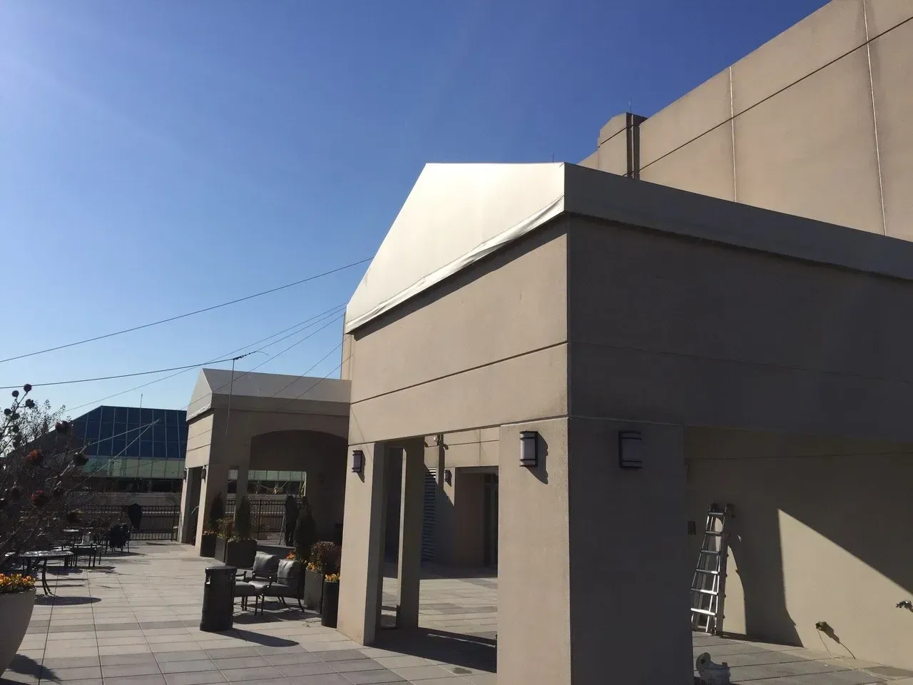 Modern gray building entrance under a clear blue sky, with a small covered walkway and parked equipment nearby