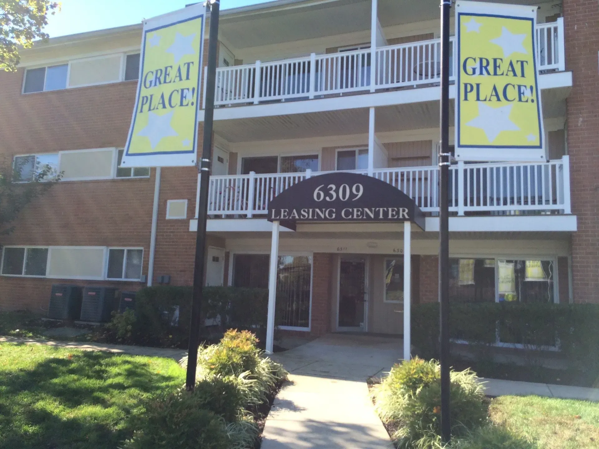 Apartment building entrance with balconies and banners reading “Great Place” and “6309 Leasing Center”