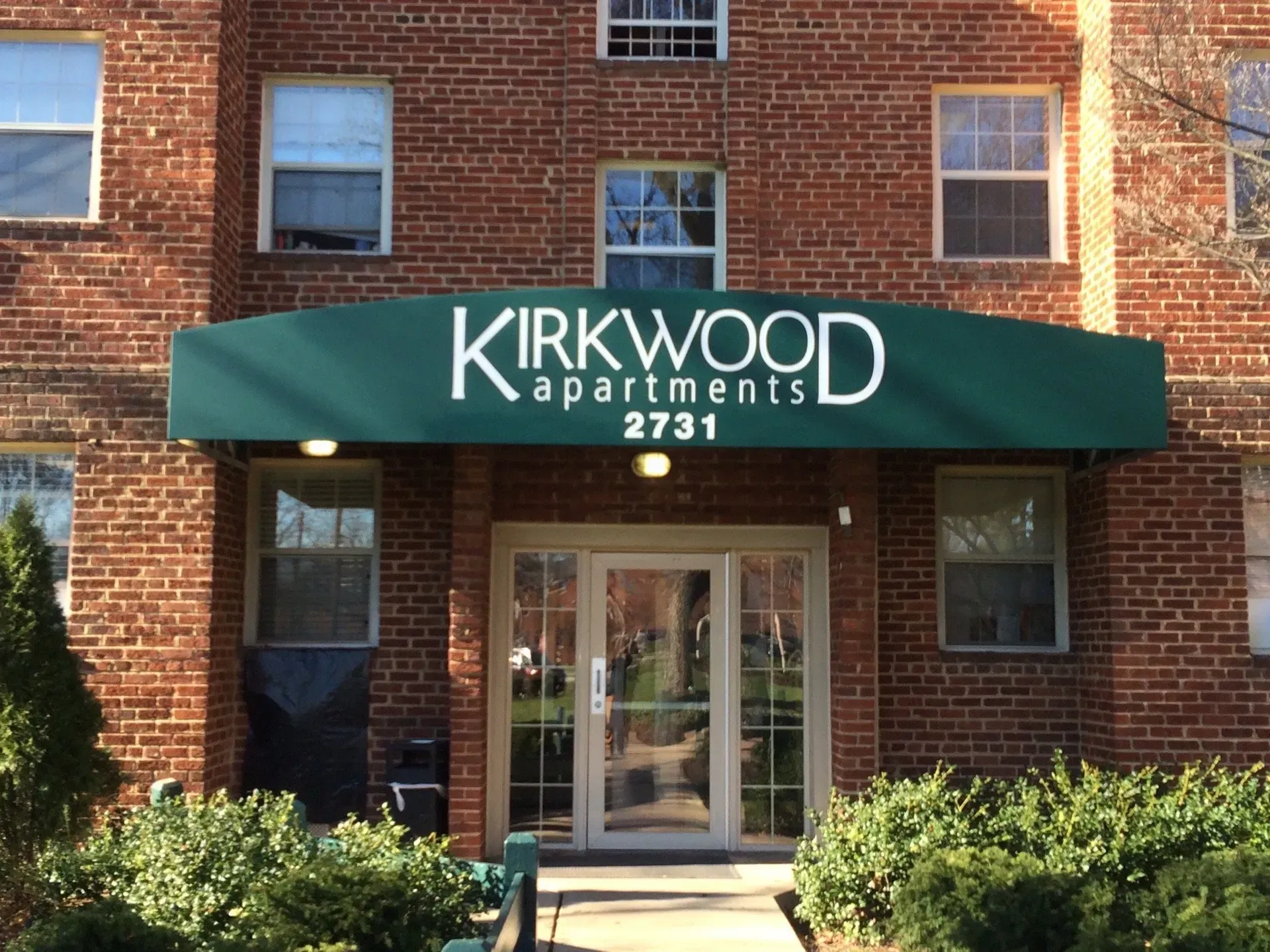 Brick apartment entrance with green awning reading “Kirkwood Apartments 2731”