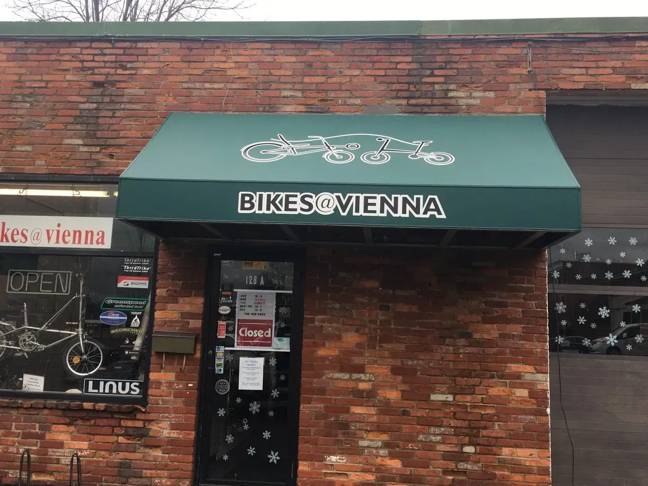 Bike shop storefront with green awning reading “BIKES VIENNA” on a brick building.