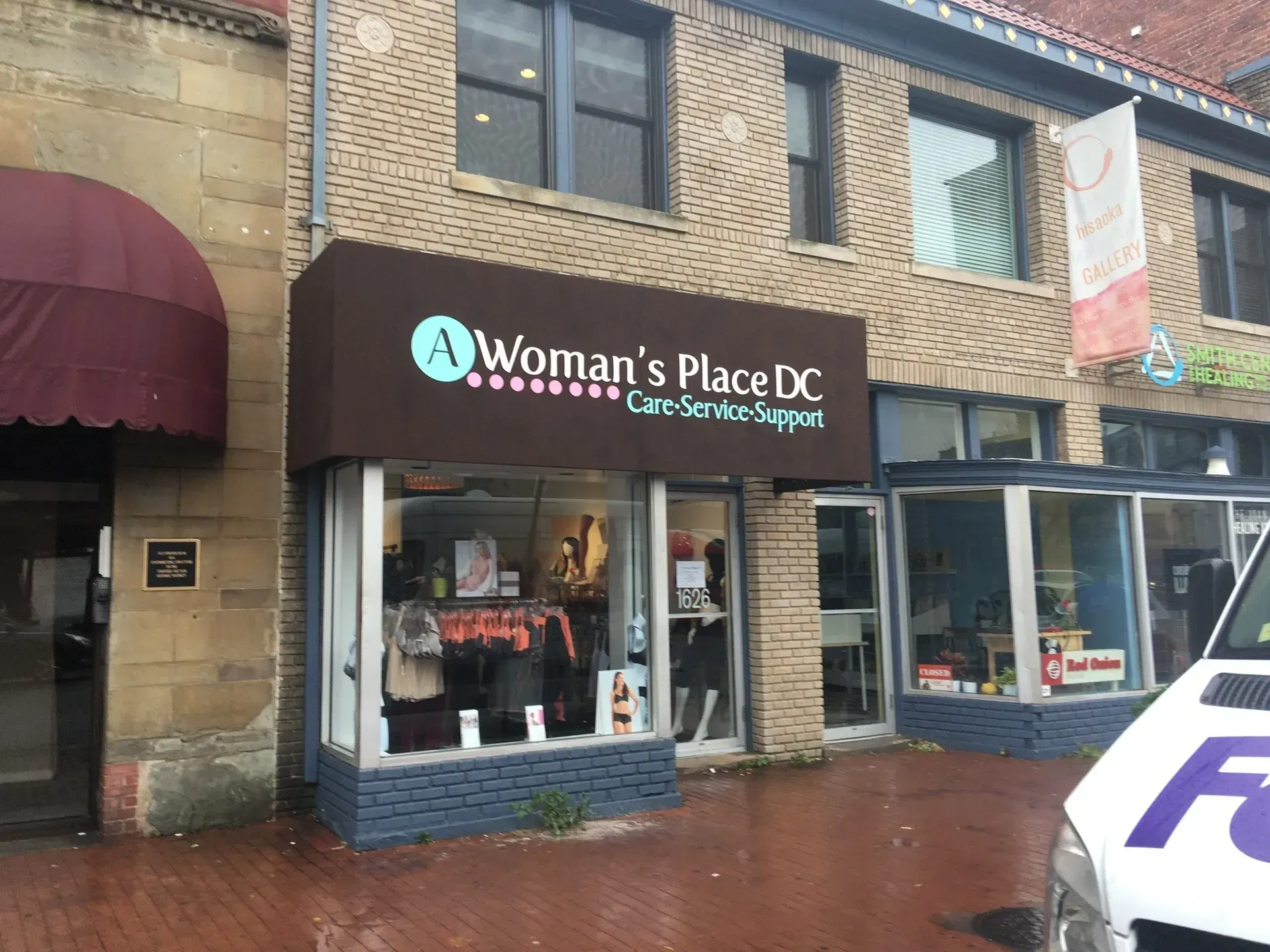 Storefront of Woman’s Place DC on a rainy brick street, with dark awning and window displays.