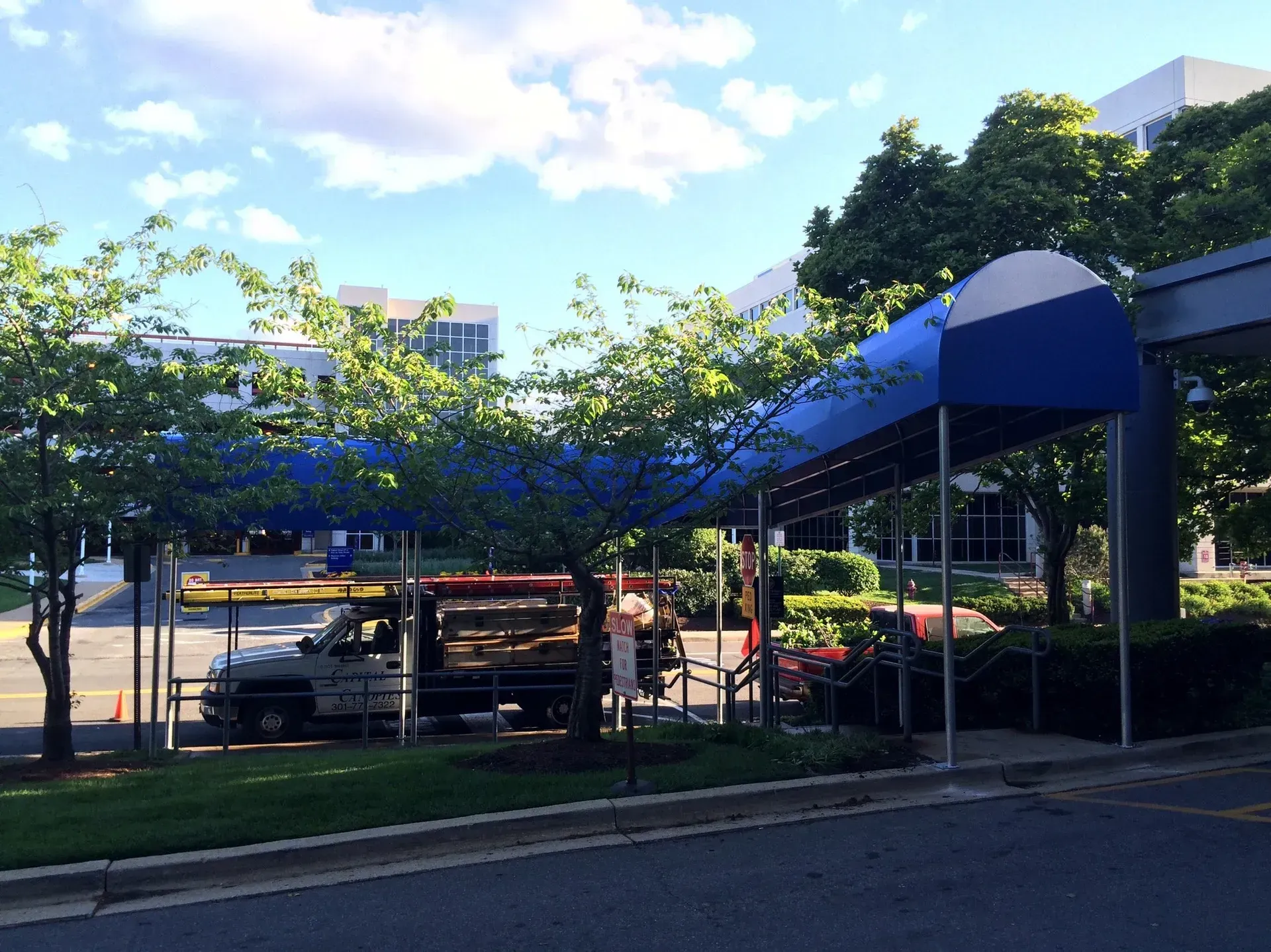 Blue canopy walkway beside parked cars and trees on a sunny day