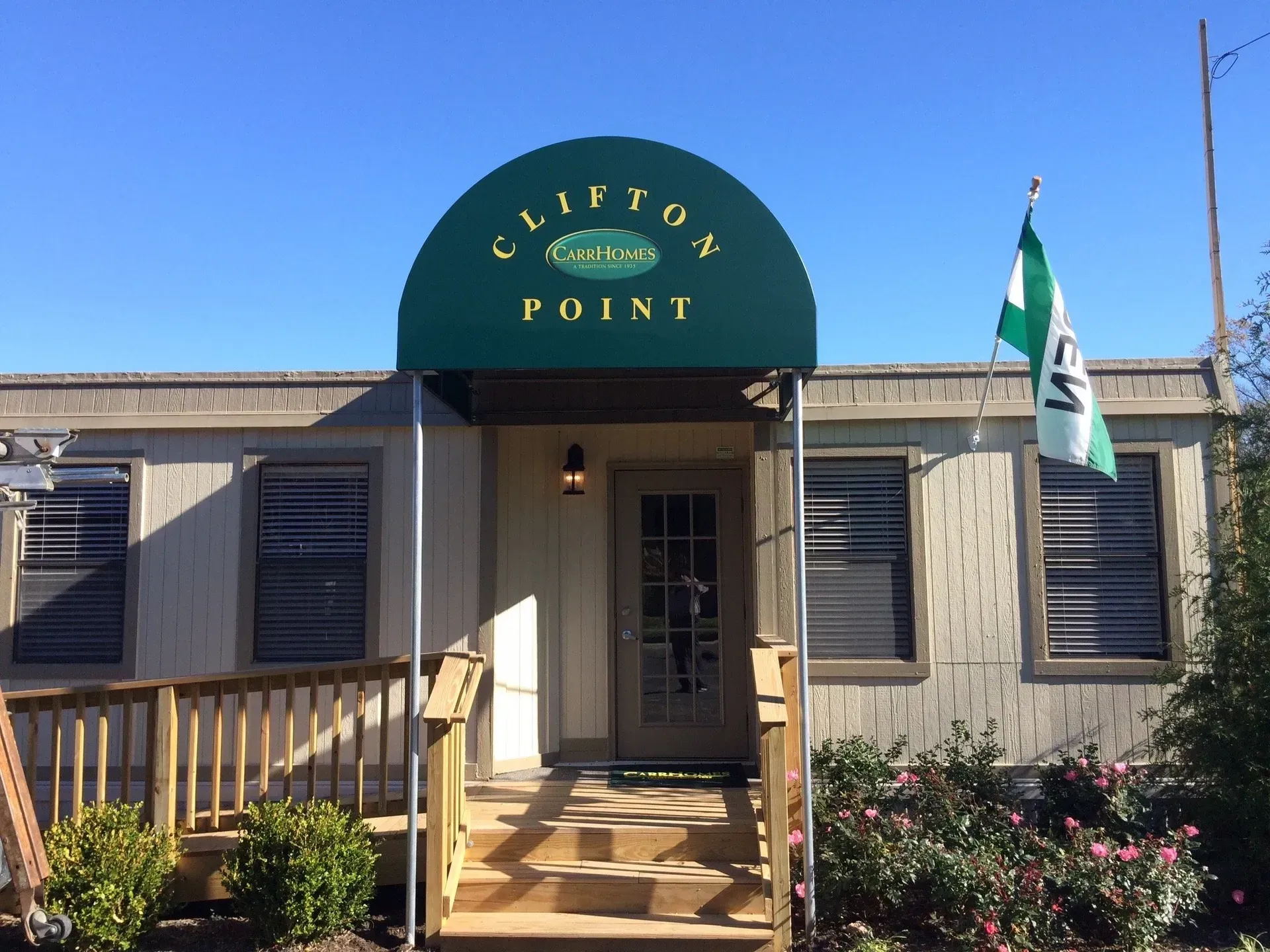 Entrance to Clifton Point with green awning, beige building, and flag by the door