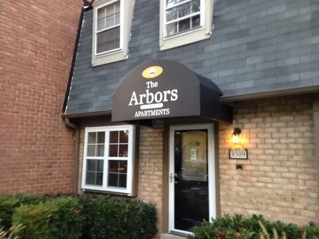 Entrance to The Arbors Apartments with dark awning and brick exterior at dusk