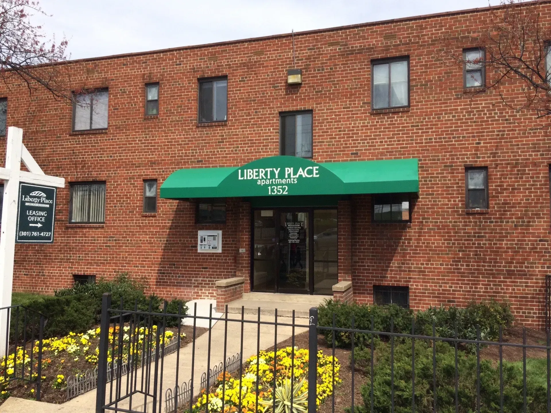 Brick building with green awning reading Liberty Place over a glass entrance and flower beds in front