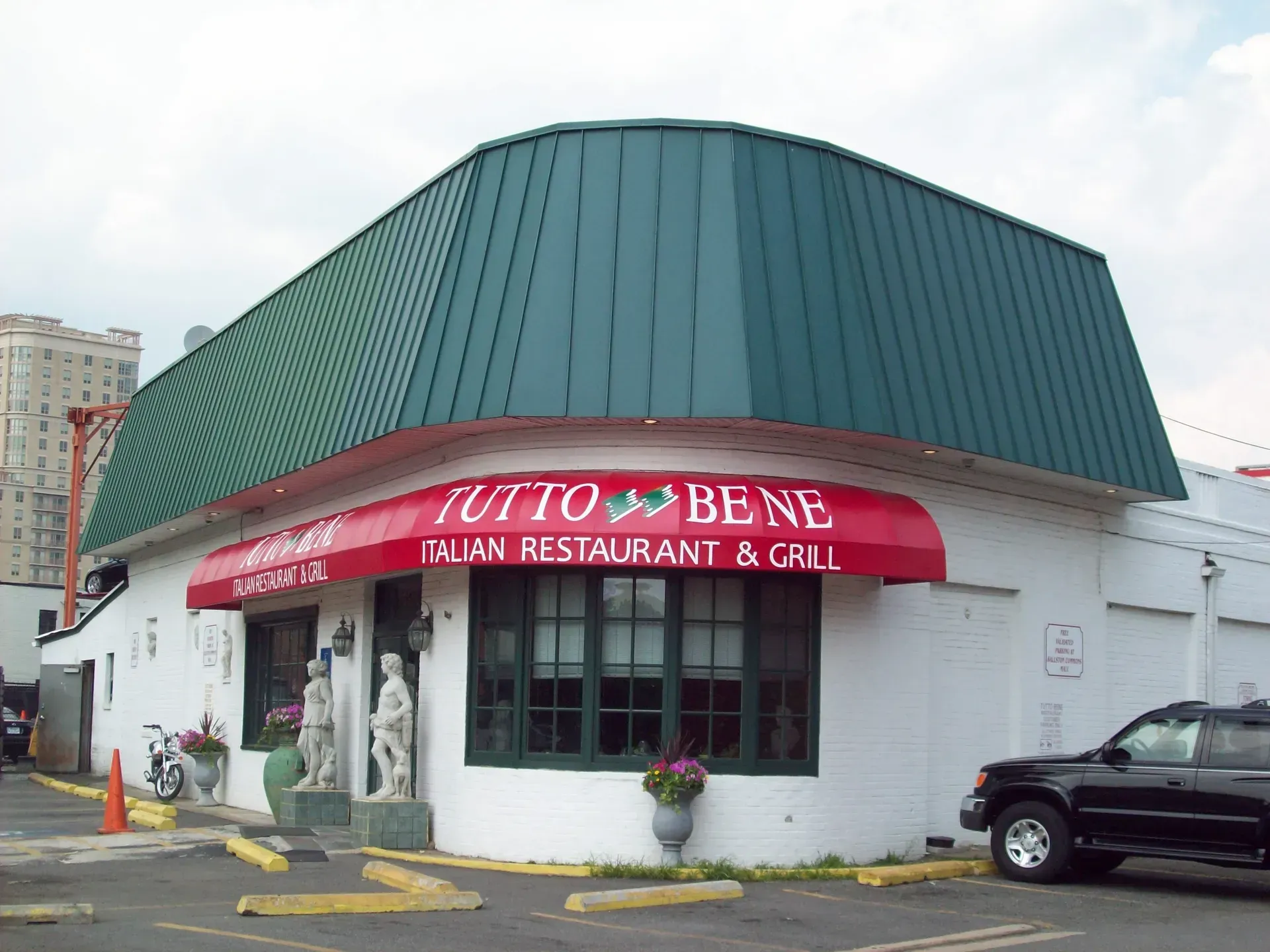 Italian restaurant with green roof, red awning, and parked car outside