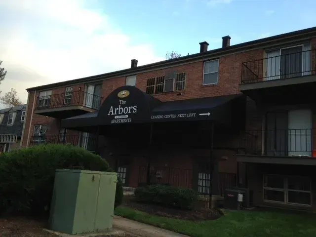 Brick apartment building with black awning for “Arbors Apartments” and balconies at dusk